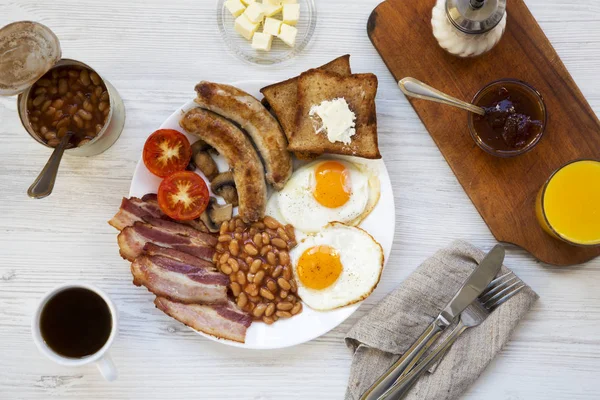 Tam İngiliz kahvaltısı kızarmış yumurta, pastırma, sosis, fasulye ve tost Beyaz ahşap arka planda, üstten görünüm ile. Düz yatıyordu. Yukarıda, ek yükü.