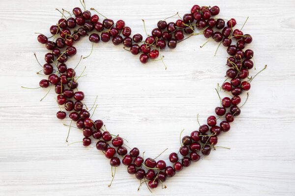 Cherries in the shape of heart on white wooden background, top view.