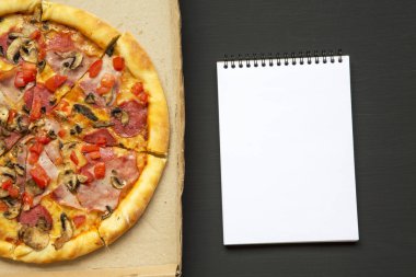 Bir karton kutu ile defter üzerinde siyah arka plan, üstten görünüm taze pişmiş pizza. Yukarıdan.