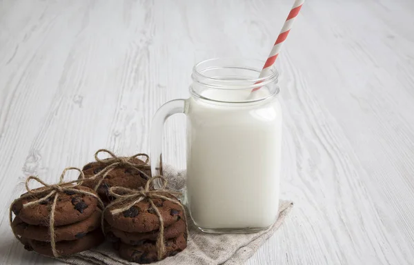 Chocolate chip cookies and jar of milk on a white wooden surface, side view. Closeup.