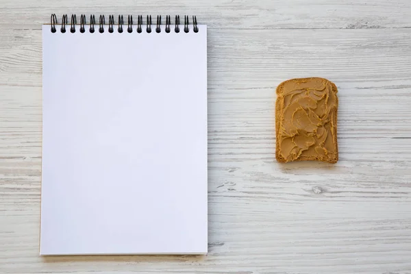 Toast Met Pindakaas Kladblok Boven Witte Houten Tafel Bovenaanzicht Van — Stockfoto