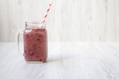 Cam kavanoz muz, siyah frenk üzümü, Hindistan cevizi sütü Beyaz ahşap yüzey, yan görünüm üzerinde yapılan güler yüzlü ile. Kopya alanı.