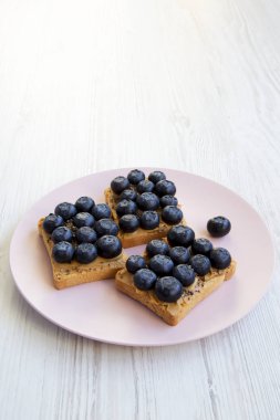 Fıstık ezmesi, yaban mersini ve beyaz ahşap arka plan, yan görünüm üzerinde pembe bir tabakta chia tohum ile tost. Sağlıklı beslenme. 