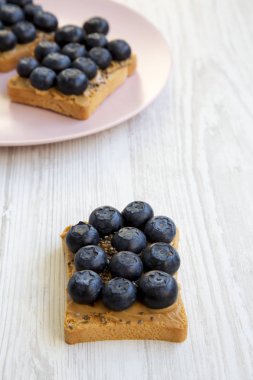 Fıstık ezmesi, yaban mersini ve beyaz ahşap yüzey, yan görünüm üzerinde chia tohum ile tost. Sağlıklı beslenme. 