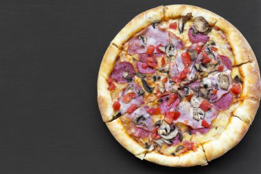 Taze pişmiş pizza düz siyah bir yüzey üzerinde yatıyordu. Uzay kopyalayın. Gelen yukarıdaki üstten görünüm.