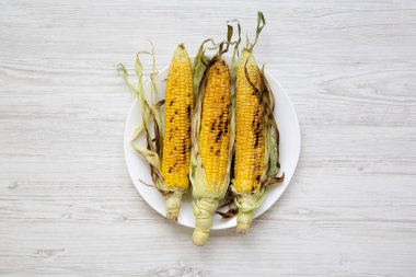 Beyaz ahşap arka plan, üstten görünüm üzerinde yuvarlak tabakta lezzetli ızgara mısır koçanı. Yukarıdan, tepegöz, düz yatıyordu.