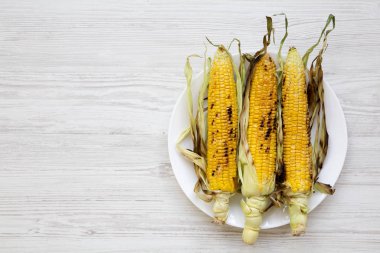 Yuvarlak tabakta Mısır koçanı Beyaz ahşap yüzeye, üstten görünüm ızgara. Yukarıdan, tepegöz, düz yatıyordu. Boşluk ve metin alanı Kopyala.