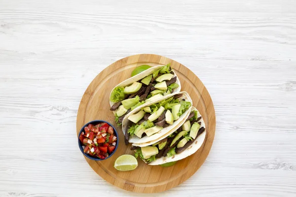 Mısır ekmeği ızgara sığır eti, avokado, kireç ve salsa ahşap tahta üzerinde yukarıda. Üstten görünüm. Kopya alanı.