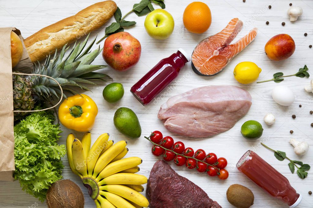 Full paper bag of various foods on a white wooden background. Close-up. Healthy eating concept. 