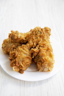 Kızarmış tavuk budu üzerinde beyaz bir plaka üzerinde ahşap yüzey, yakın çekim beyaz. Yan görünüm.