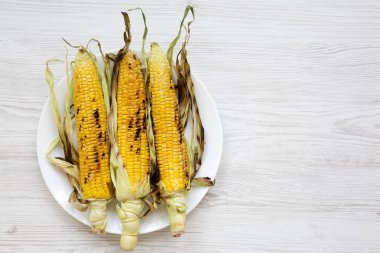 Izgara Mısır bir beyaz yuvarlak tabak Beyaz ahşap arka plan üzerinde üstten görünüm. Yaz vegan Aperatif. Sağlıklı beslenme. Kopya alanı.