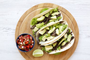 Mısır ekmeği ızgara sığır eti, avokado, kireç ve salsa bir yuvarlak bambu tahta üzerinde. Yukarıdan, ana sayfa görünümü.