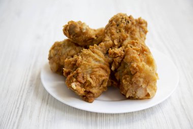 Kızarmış tavuk budu üzerinde beyaz bir tabak Beyaz ahşap yüzeye, closeup yuvarlak. Yan görünüm.