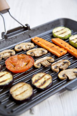 Beyaz ahşap zemin, yan görünüm üzerinde ızgara bir tavada ızgara sebze. Yakın çekim. 