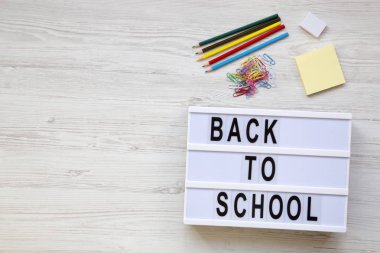 Eğitim kavramı. Silgi, kurşun kalem, çıkartmalar, ataç ve 'Back to school' kelime bir beyaz tahta yüzey üzerinde modern bir gemide. Yukarıda, ek yükü. Kopya alanı.