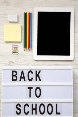 Tablet, silgi, kurşun kalem, çıkartmalar, ataç ve 'okula geri' kelime beyaz ahşap masa üzerinde modern bir gemide. Gelen yukarıdaki üstten görünüm.