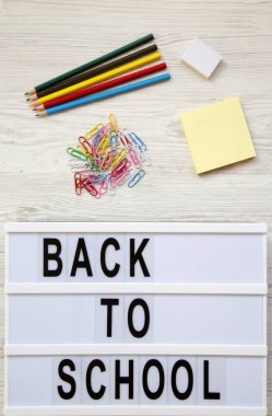 Eğitim kavramı. Silgi, kurşun kalem, çıkartmalar, ataç ve 'Back to school' kelime beyaz ahşap zemin üzerinde modern bir gemide. Gelen yukarıdaki üstten görünüm.