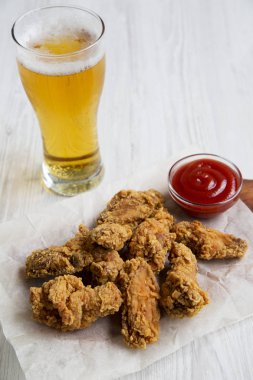 Soslu kızarmış tavuk kanatları, bir beyaz tahta arka planda soğuk bira yakın çekim. 