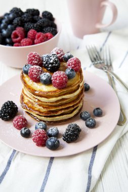 Tablo, yan görünüm pembe plaka farklı meyveler ile Pancakes.