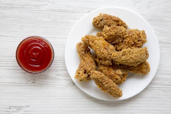 Üstten görünüm Beyaz ahşap arka plan üzerinde kırmızı biber soslu yuvarlak beyaz tabakta tavuk kanatları. Yakın çekim.