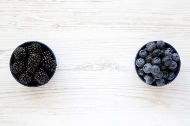 Olgun böğürtlen ve yaban mersini Beyaz ahşap masa, üstten görünüm üzerinde mavi kase. Yaz meyve. Yukarıdan, düz, ek yükü. Metin için yer.