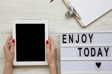 Tablet, Not defteri ve 'bugün zevk' kelime lightbox ile alan beyaz ahşap zemin, üstten görünüm üzerinde çalışıyorum. Eller tablet boş ekran ile tutun. Yukarıdan, düz-lay, tepegöz. 