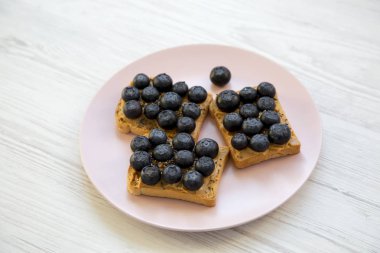 Fıstık ezmesi, yaban mersini ve beyaz ahşap arka plan, yüksek açı üzerinde pembe bir tabakta chia tohum ile vejetaryen tost. Sağlıklı beslenme ve diyet. 