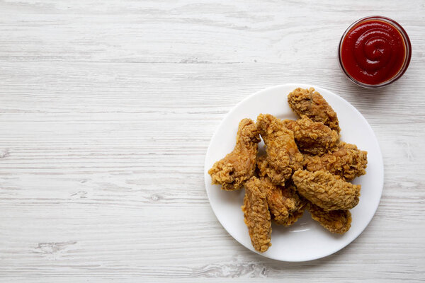 Куриные крылья на круглой белой тарелке с соусом над белой деревянной поверхностью, вид сверху. Сверху, плоский лежал, вид сверху. Копирование пространства и текста
.