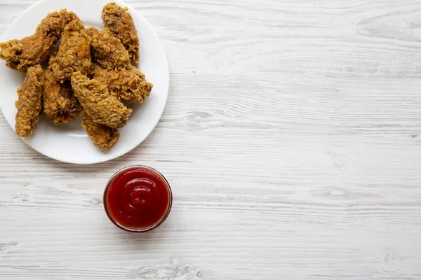 Beyaz ahşap arka plan, üstten görünüm üzerine ketçap ile yuvarlak beyaz tabakta tavuk kanatları. Düz, tepegöz, yukarıdan yatıyordu. Metin için yer.