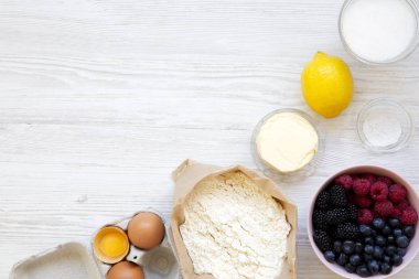 Üstten görünüm, berry pie bir beyaz tahta yüzey üzerinde yemek pişirmek için ham maddeler. Düz lay, ek yükü. Kopya alanı.