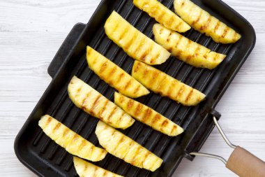 Beyaz ahşap zemin üzerinde ızgara tavada ızgara ananas dilimleri görüntüleme yukarıdan. Yaz yiyecek. Portre. Tepegöz, yat.