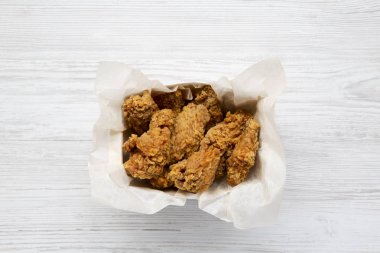 Beyaz ahşap bir masa, ek yükü kağıt kutusunda tavuk kanatları. Düz yatıyordu, en iyi görünüm. Yakın çekim.