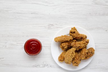Beyaz ahşap bir masa üstten görünüm ketçap ile yuvarlak beyaz tabakta tavuk kanatları. Düz, tepegöz, yukarıdan yatıyordu. Kopya alanı.