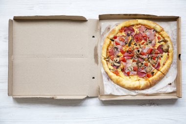 Beyaz ahşap masa, üstten görünüm üzerinde bir karton kutu içinde taze pizza. Yukarıdan, lay düz.