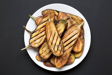 Yukarıdan görünüm, siyah arka plan üzerinde beyaz bir plaka üzerinde ızgara patlıcan. Portre.