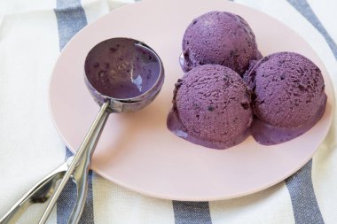 Yaban mersini dondurma dondurma kaşık çizgili peçete, yan görünüm üzerinde pembe bir tabakta toplarla. Portre.