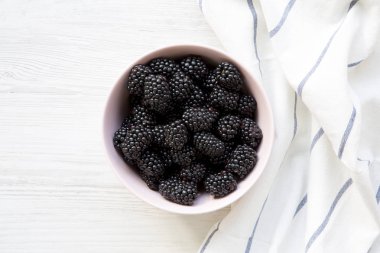 Beyaz ahşap bir masa, üstünde pembe kase taze böğürtlen görüntülemek yukarıdan.