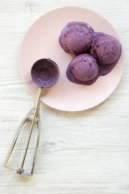 Yukarıdan, yaban mersini dondurma top dondurma ile beyaz ahşap arka plan üzerinde pembe bir plaka üzerinde kepçe. Yakın çekim.