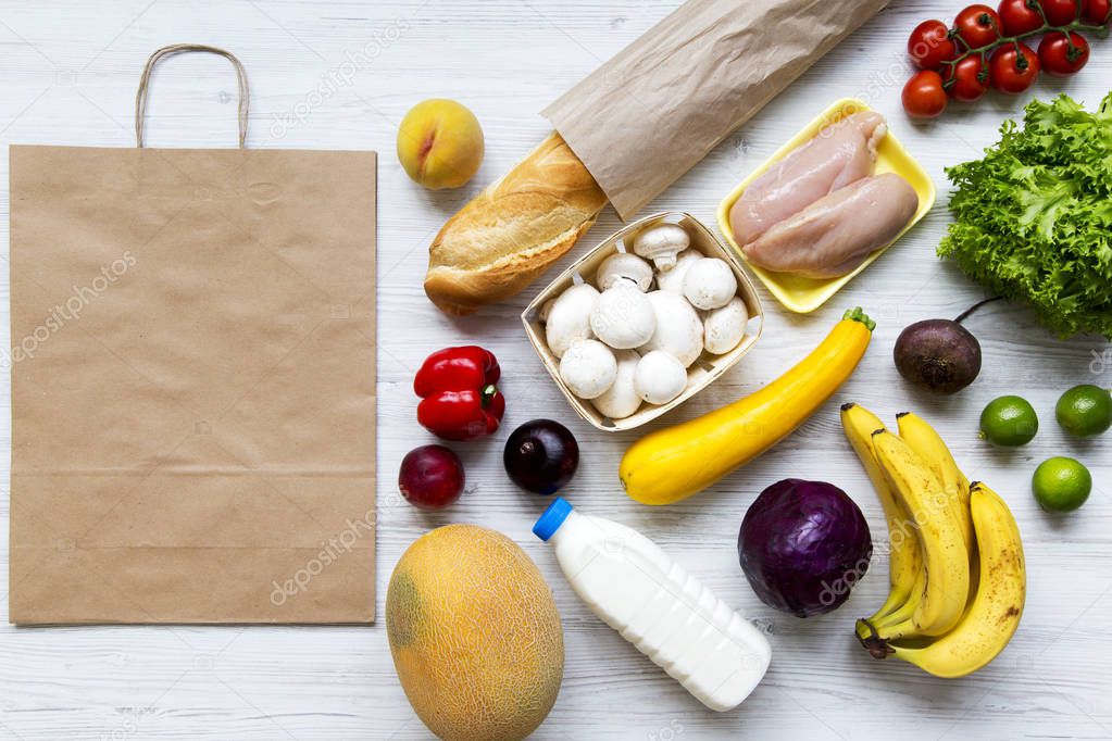 Paper bag of health raw food on white wooden background. Cooking food background. Flat-lay of fresh fruits, veggies, greens, chicken breast, top view. Shopping concept.