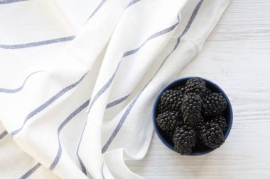 Böğürtlen ile çizgili beyaz ahşap masa, üstten görünüm peçeteye tam seramik kase. Yaz meyve. Yukarıda, ek yükü. 