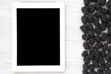 Beyaz ahşap masa, üstten görünüm tablete ile böğürtlen. Yaz meyve. Boş ekran.