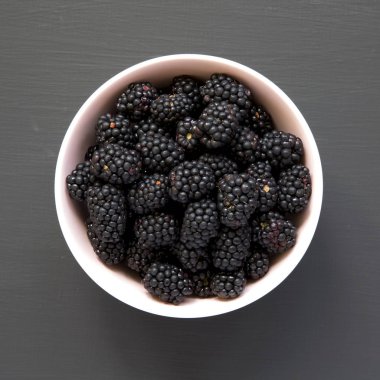 Böğürtlen siyah arka plan, üstten görünüm üzerinde pembe kase. Yaz meyve. Yukarıda, ek yükü. Portre.