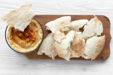 Leblebi, kırmızı biber, zeytin yağı ve pide ekmek üzerinde beyaz ahşap tablo., üstten görünüm rustik ahşap tahta üzerinde humus kase. Yukarıda, ek yükü. Portre.