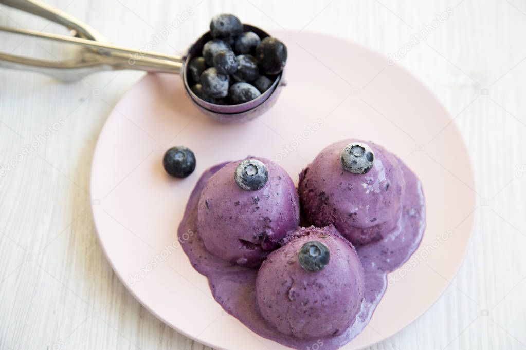 Blueberry ice cream balls with icecream scoop on a pink plate over white wooden suface, closeup.