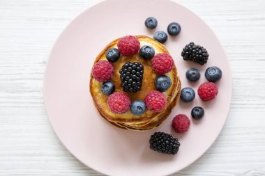 Beyaz ahşap masa, üstten görünüm üzerinde pembe bir plaka üzerinde meyveleri ile Pancakes. 