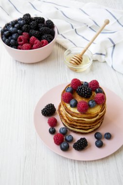 Çilek ve beyaz ahşap yüzey, yüksek açı üzerinde pembe bir tabakta bal ile Pancakes.