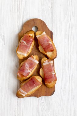 Crostini ile serrano jambonu Beyaz ahşap zemin üzerinde rustik ahşap tahta üzerinde ana sayfa görünümü.