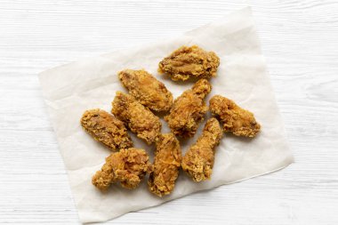 Kağıt tepsisine Beyaz ahşap arka plan üzerinde üstten görünüm üzerinde kızarmış tavuk kanatları. Yukarıda, ek yükü. 