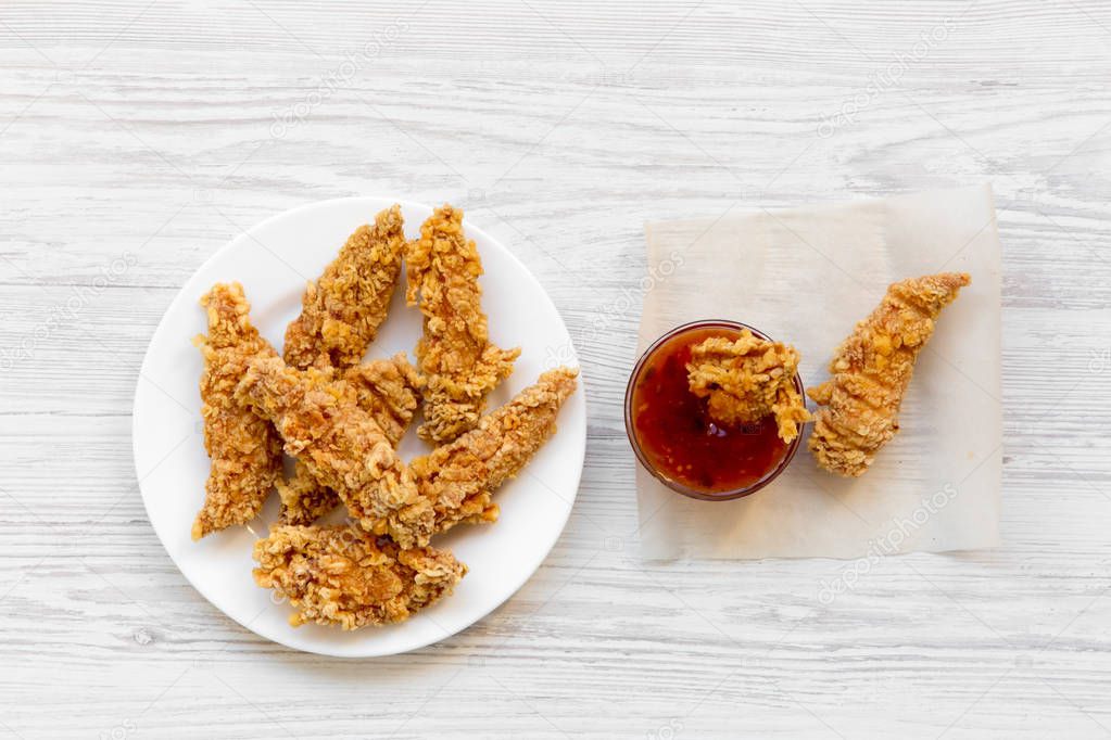 Spicy chicken strips on white plate with sauce over white wooden background, top view. Flat lay, from above, overhead. Closeup.