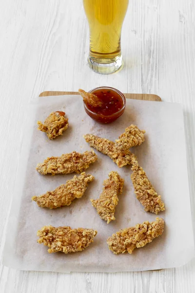 Chicken fingers with sauce and beer over white wooden background, high angle.